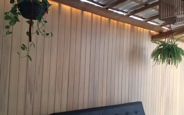 Revestimento de parede em PVC amadeirado com fita de LED em área de lazer com pergolado